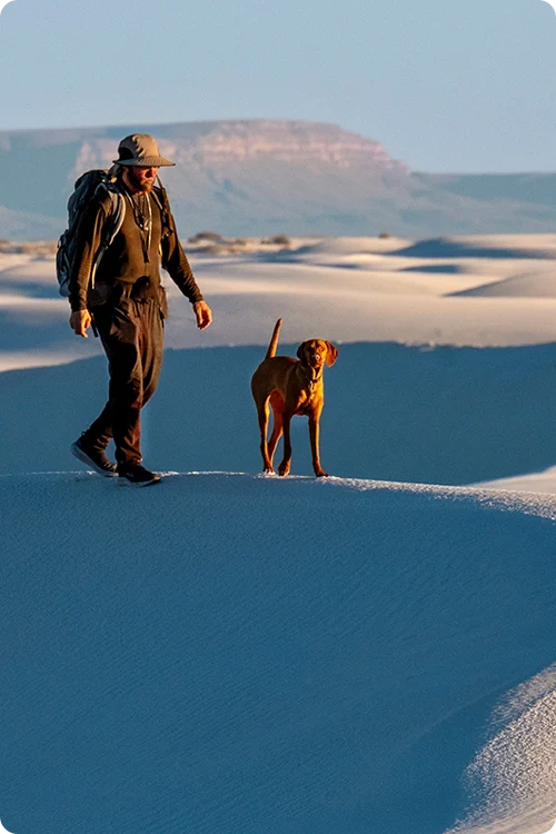 Man walking with his dog through white sand